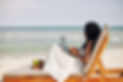 Young woman enjoying sitting on chaise-lounge, working on laptop and looking on sea waves.